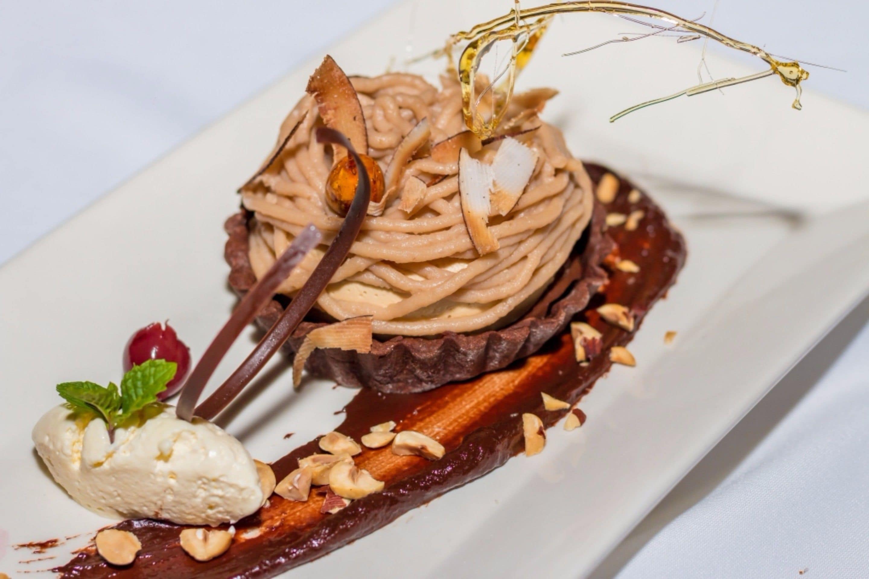Postre con mousse de chocolate, nueces y una guarnición de menta sobre un plato blanco.