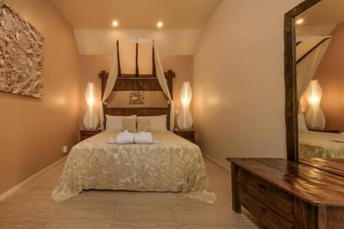 Un dormitorio con cama a dosel, lámparas de noche, cómoda de madera y un espejo grande.
