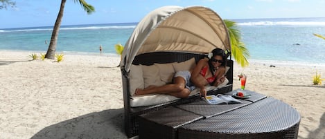 A beachside lounge with a covered seating area, a wicker table, and a view of the ocean.