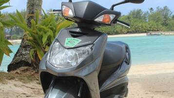 A scooter parked on a sandy beach with a palm tree and clear blue water in the background.
