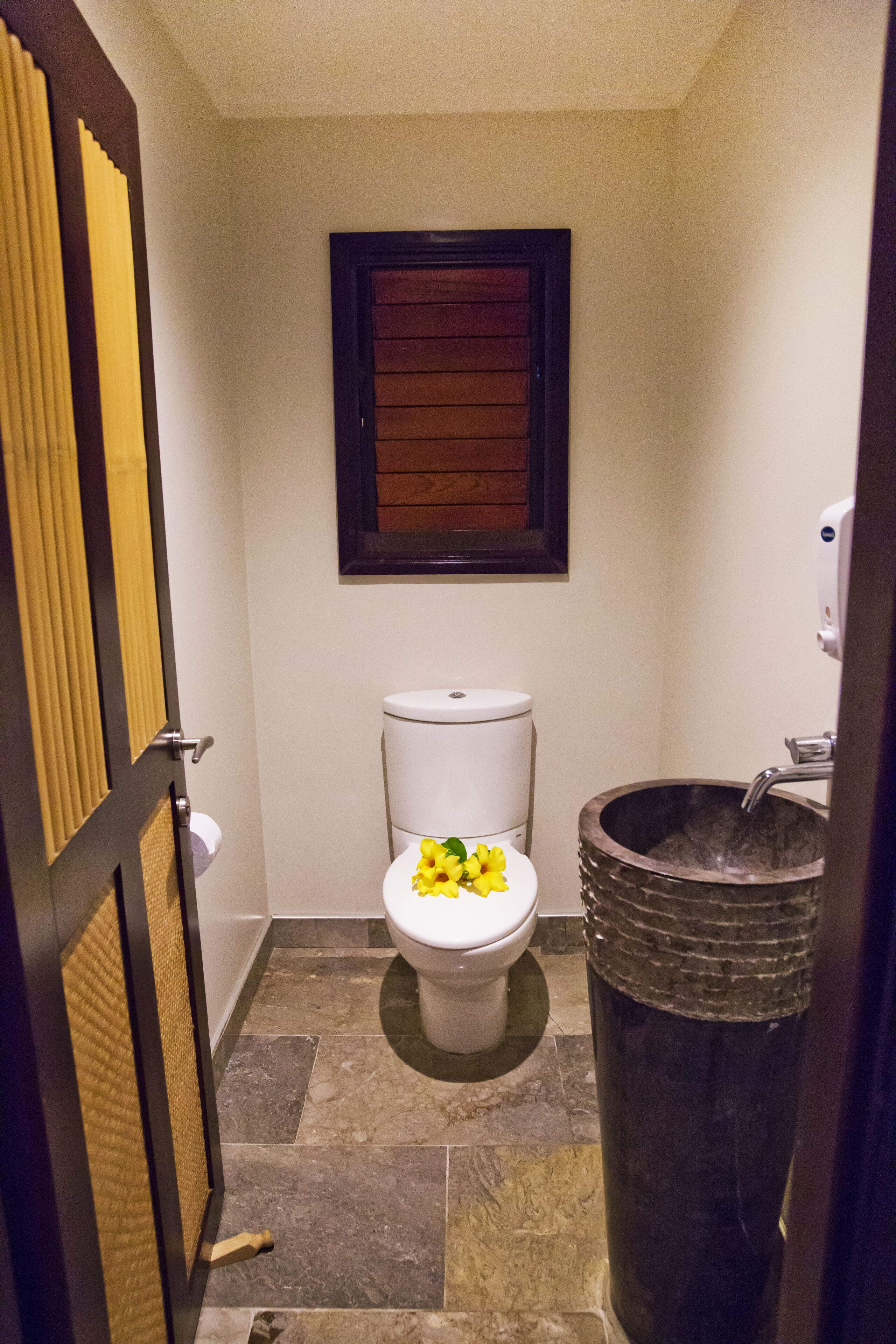 A small bathroom with a toilet, a wooden-framed window, and a sink with a unique basin.