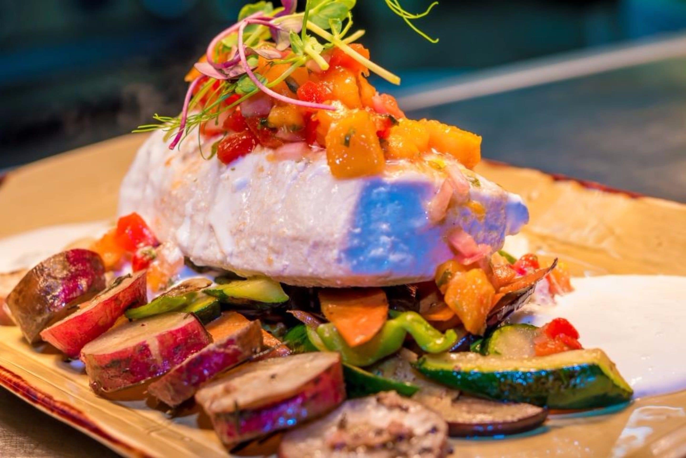 A plate with a fish fillet, roasted vegetables, and a salsa topping.
