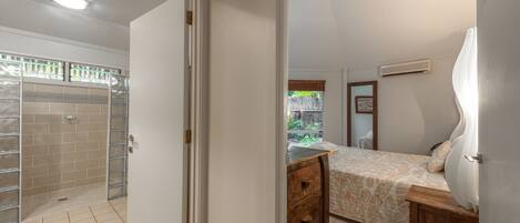 A bedroom with a bed, a wooden nightstand, a dresser, and a window with a view of greenery.