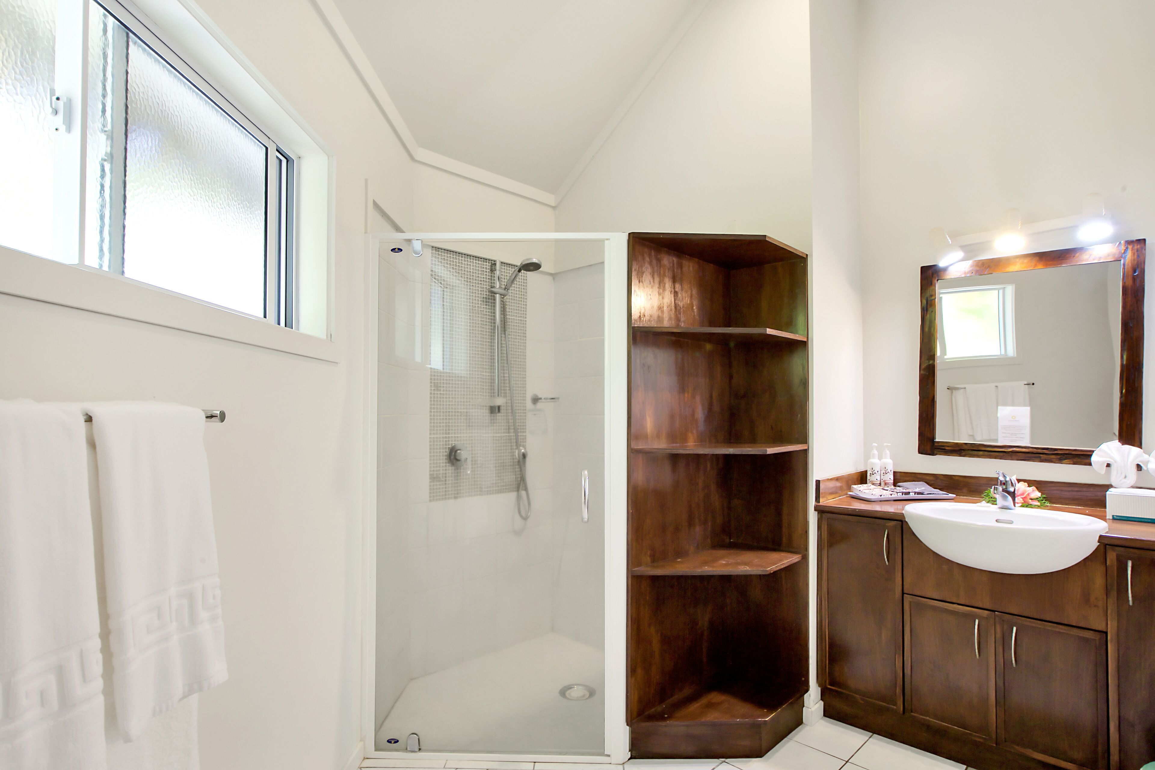 A bathroom with a glass-enclosed shower, wooden shelves, a sink, and a mirror.