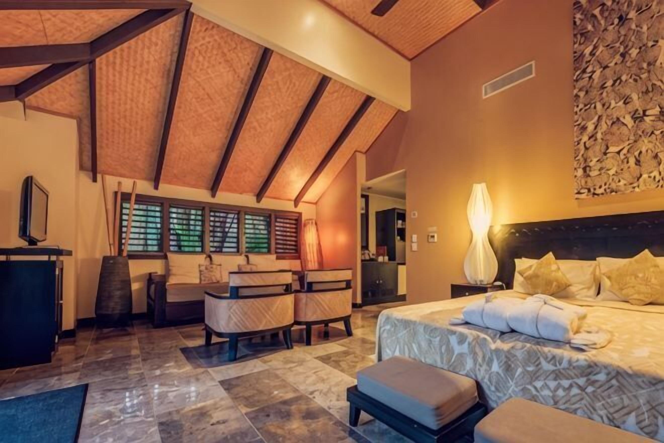 A bedroom with a bed, bedside table, lamp, and a desk with a chair.