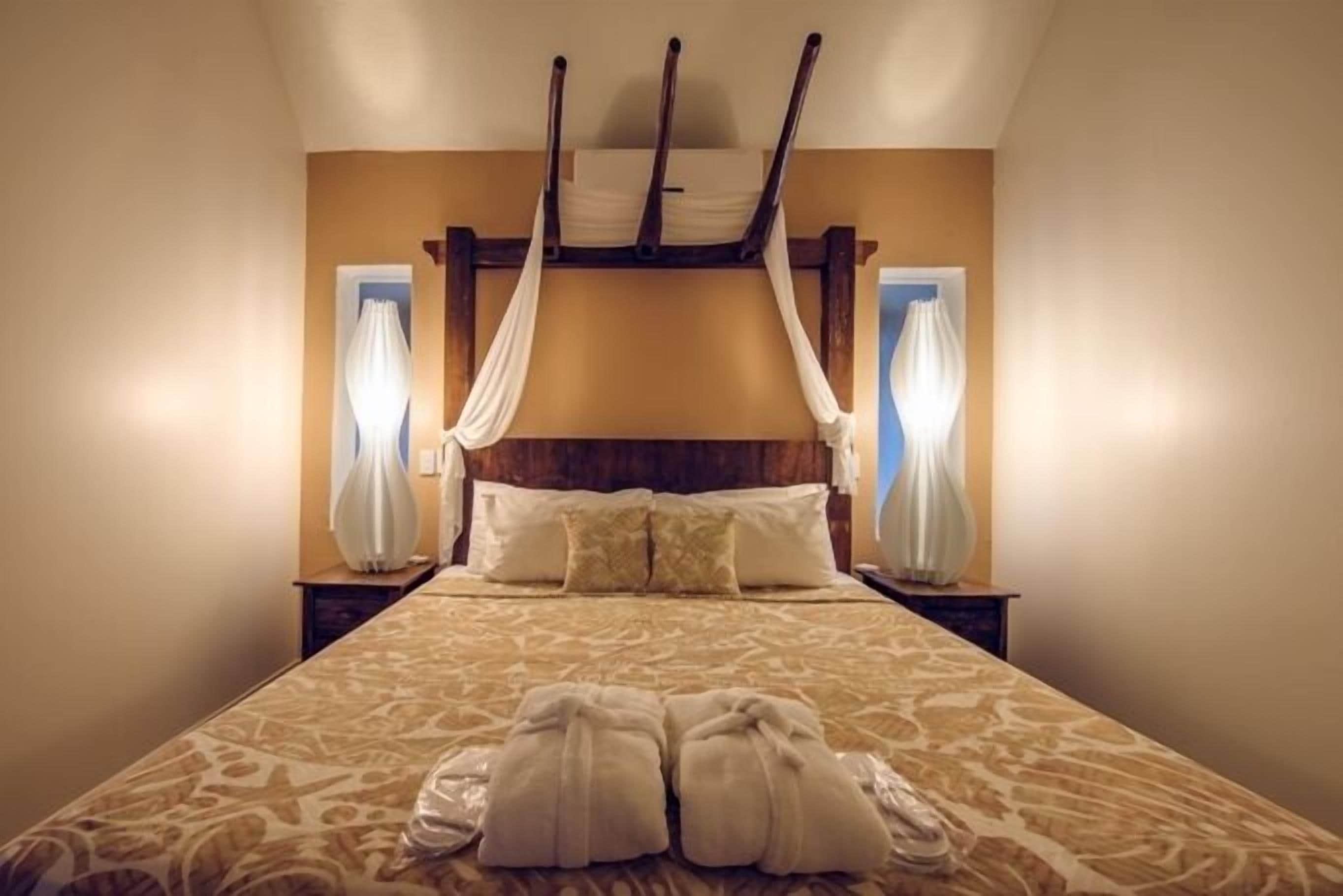 Een bed met hemelbed, twee nachtkastjes met lampen, en een paar handdoeken op het bed.