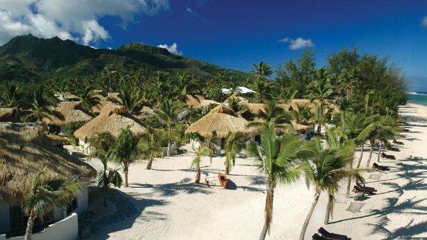 A beach with thatched-roof huts, palm trees, and clear turquoise waters. - Crown Beach Resort & Spa (Rarotonga)