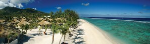 A beach with thatched-roof huts, palm trees, and clear turquoise waters. - Crown Beach Resort & Spa (Rarotonga)