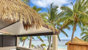 A beachside patio with a thatched roof, white outdoor furniture, and a view of the ocean. - Crown Beach Resort & Spa (Rarotonga)
