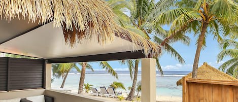 Un patio frente a la playa con techo de paja, muebles de exterior blancos y vista al océano.