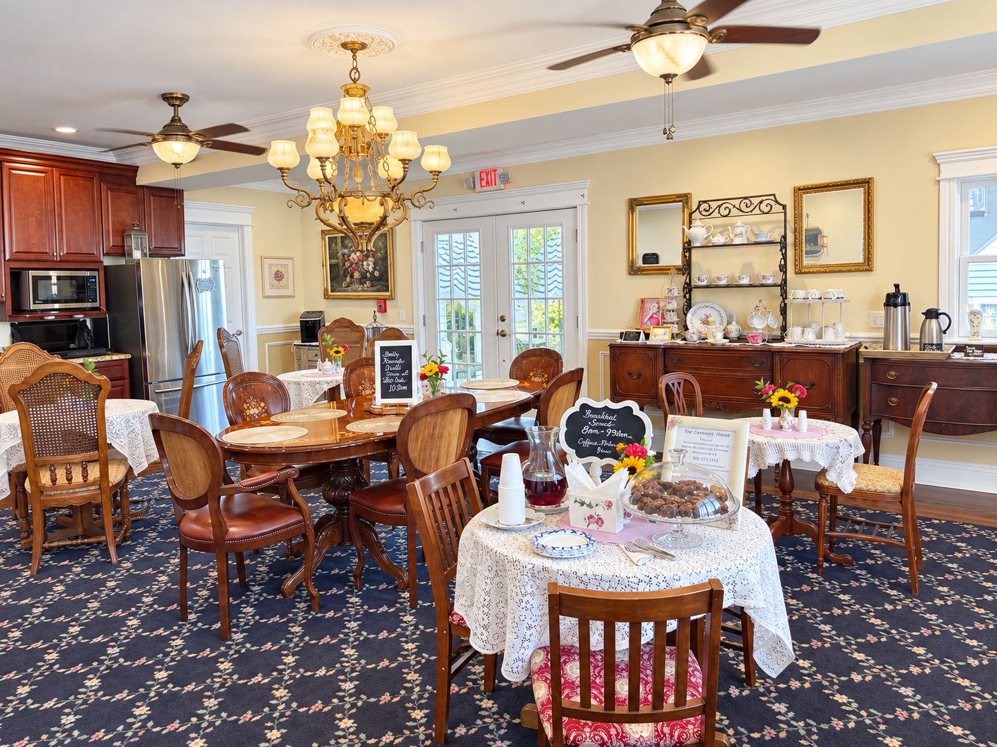 A dining area with a chandelier, wooden chairs, a table with a lace tablecloth, and a floral carpet.