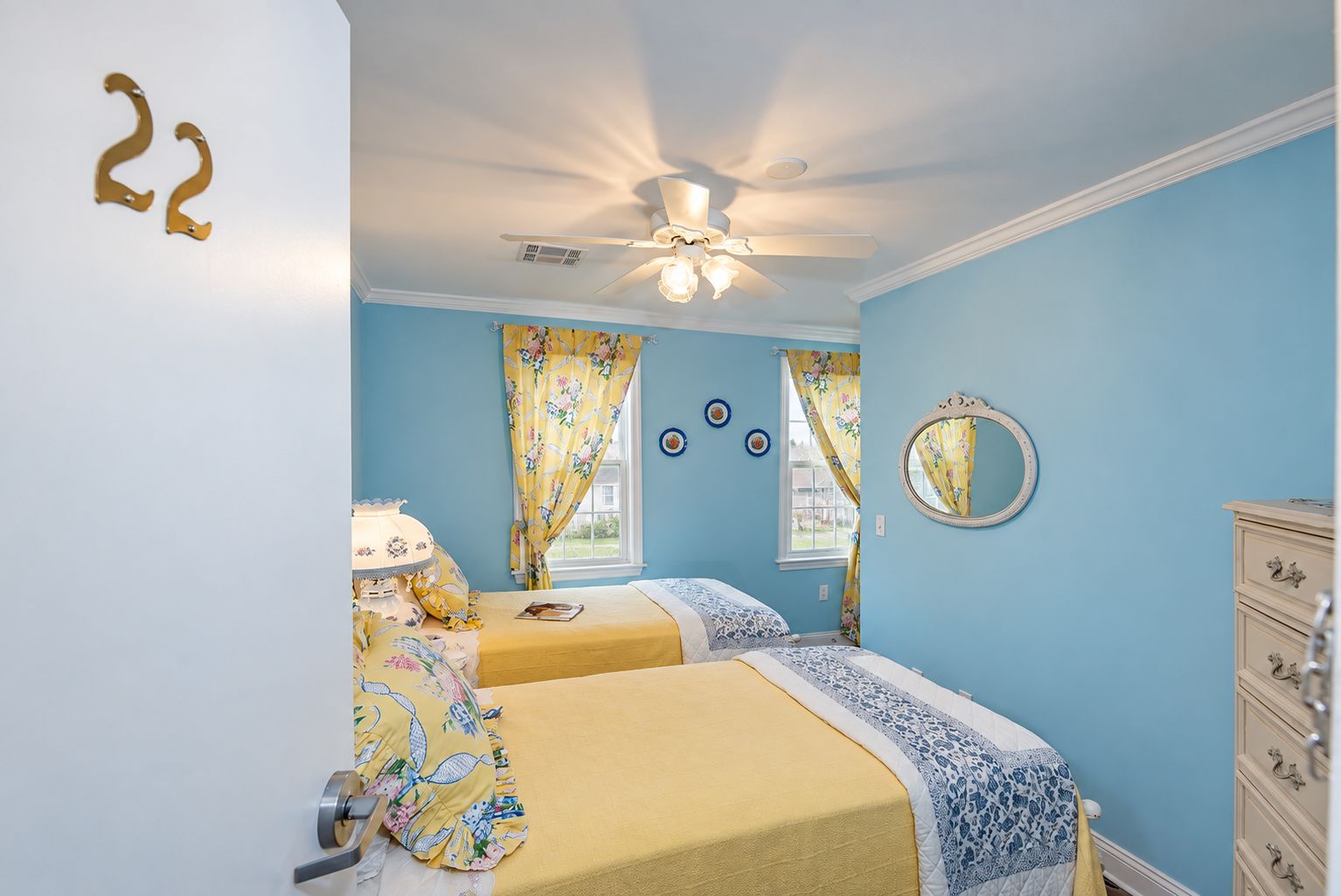 Une chambre avec deux lits, un ventilateur de plafond, une commode et une fenêtre avec des rideaux.