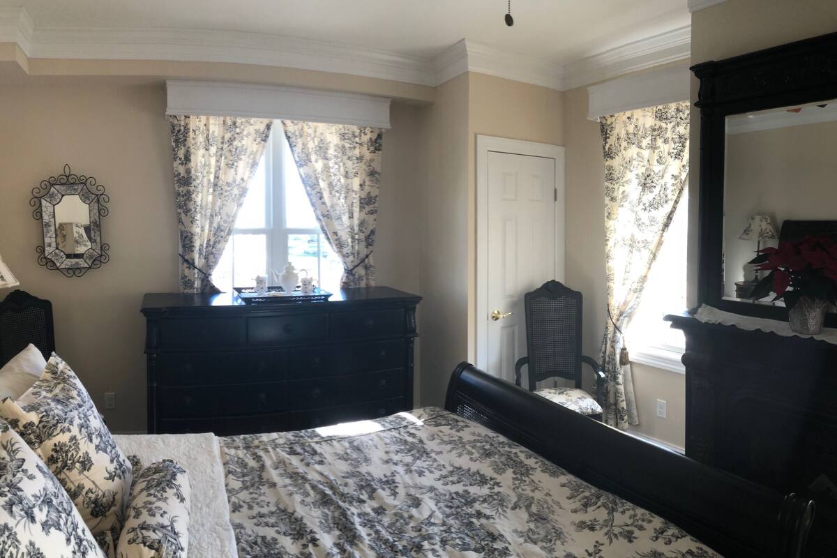 A bedroom with a bed, dresser, mirror, and window with curtains.