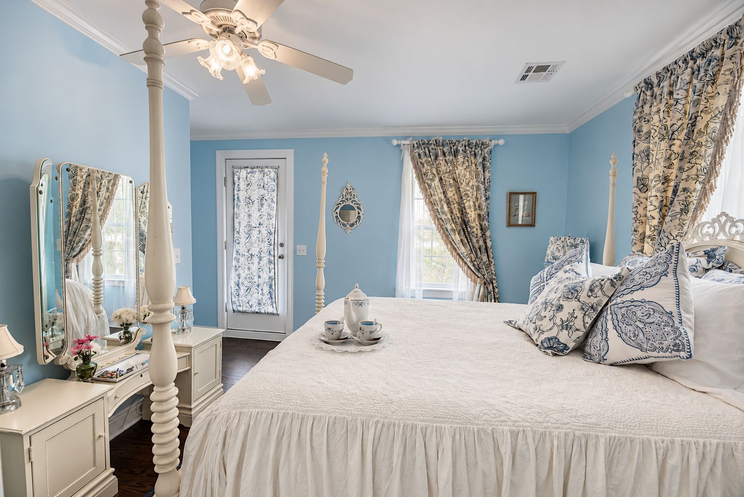 A bedroom with a four-poster bed, a ceiling fan, and a window with patterned curtains.