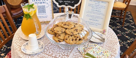 A table with a glass pitcher of iced tea, a bowl of cookies, a sign for breakfast service, and a welcome sign for The Carriage House.