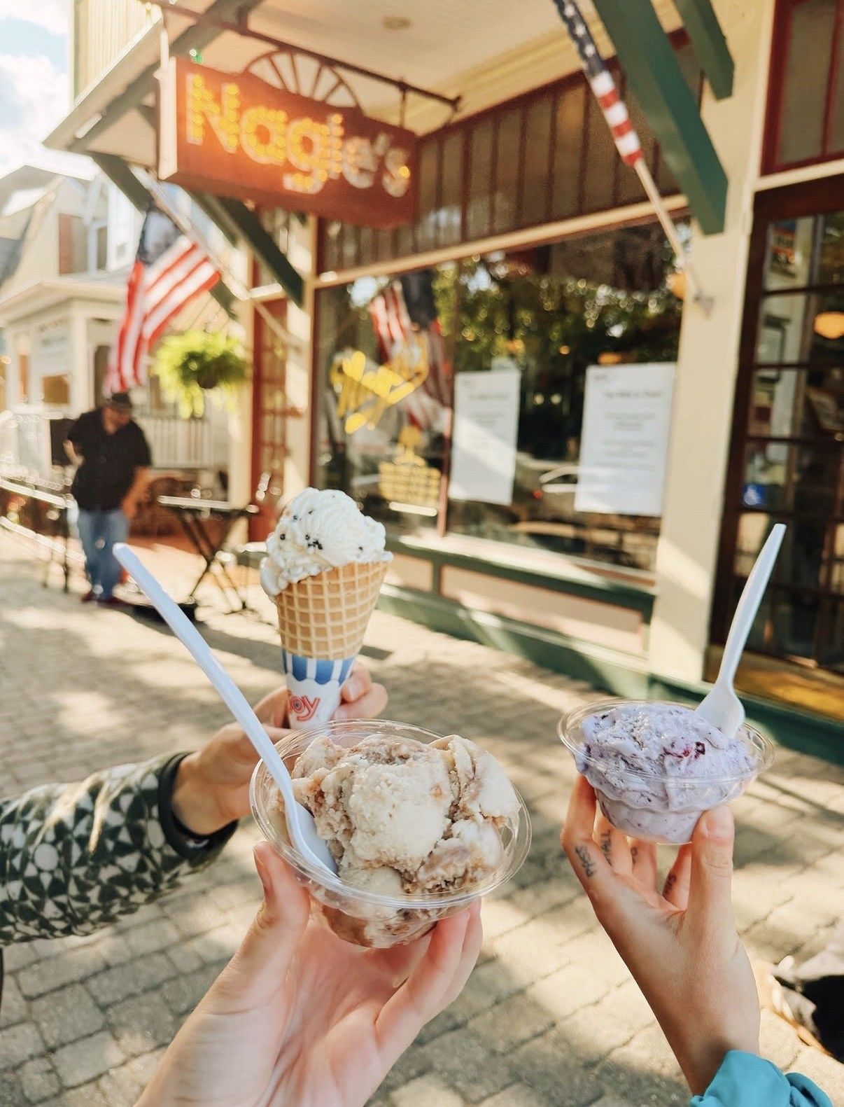 A person holding two ice cream cones and a cup of ice cream.