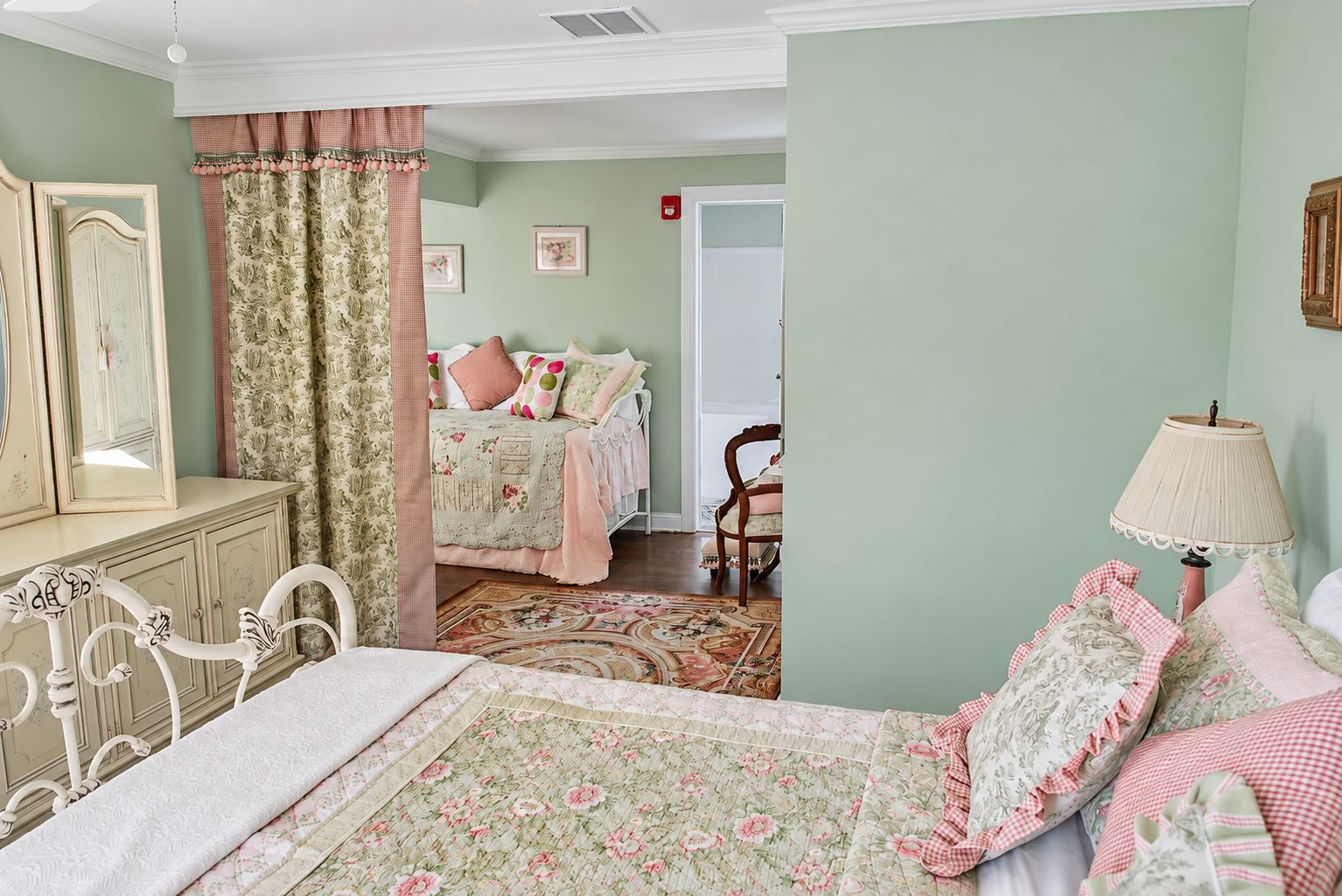 A bedroom with a bed, dresser, mirror, and a chair.