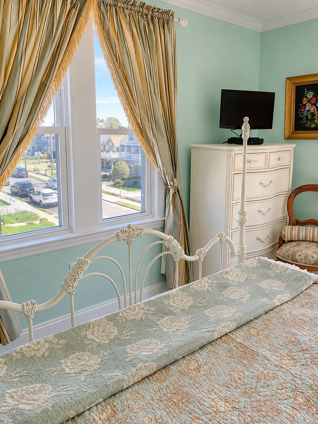 A bedroom with a bed, a dresser, a television, and a window with curtains.