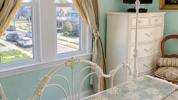 A bedroom with a bed, a dresser, a television, and a window with curtains.
