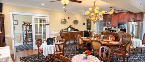 A spacious dining area with multiple tables and chairs, a ceiling fan, and a kitchen area with wooden cabinets and appliances.
