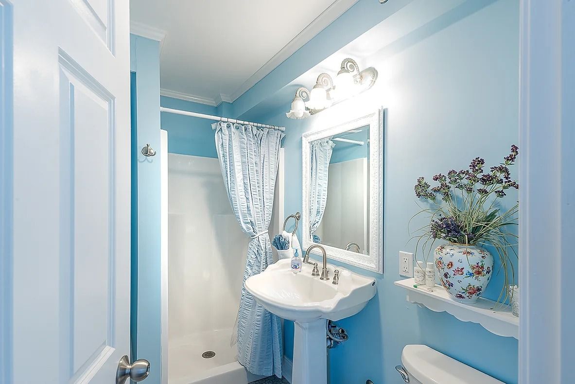 A bathroom with a white sink, a mirror, a shower curtain, and a vase with flowers.
