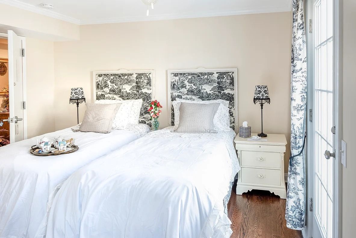 Un dormitorio con dos camas, una mesita de noche con lámpara y una ventana con cortinas.