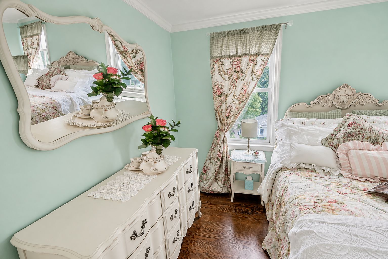 Un dormitorio con cama, cómoda, espejo y ventana con cortinas.