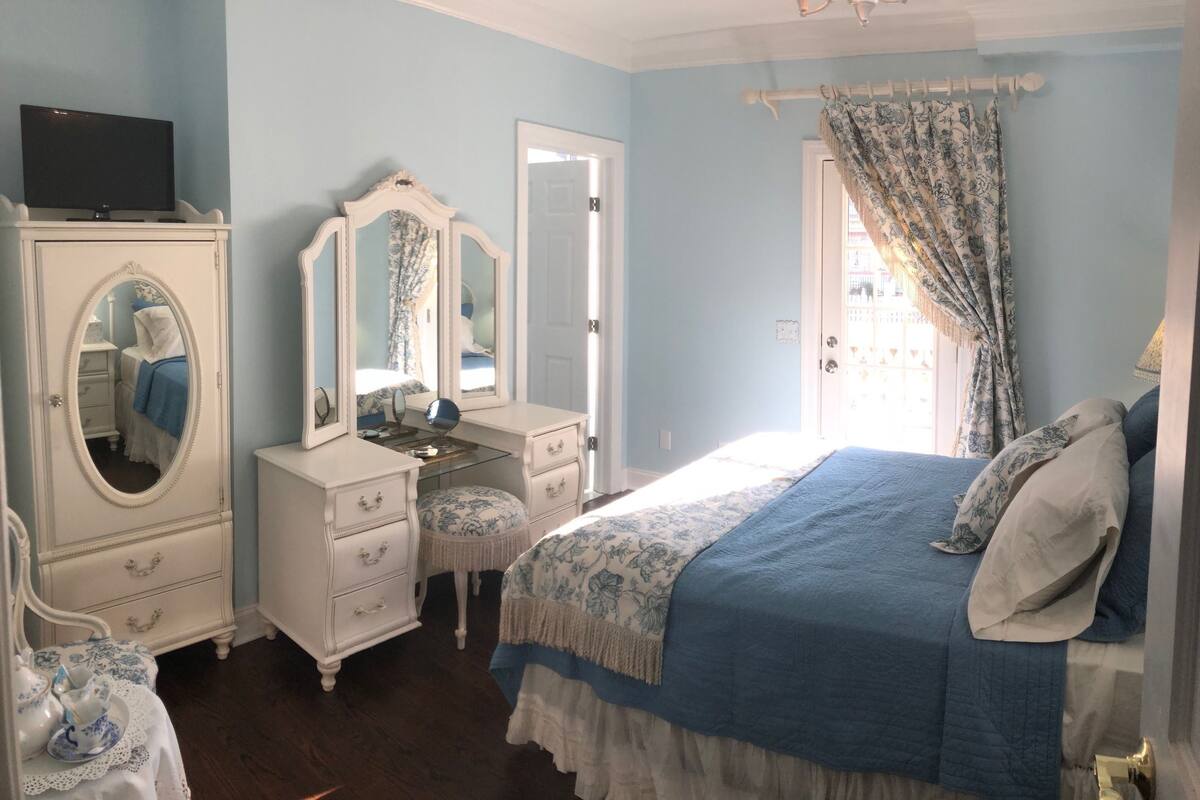 A bedroom with a bed, dresser, vanity with mirror, and a television on a cabinet.