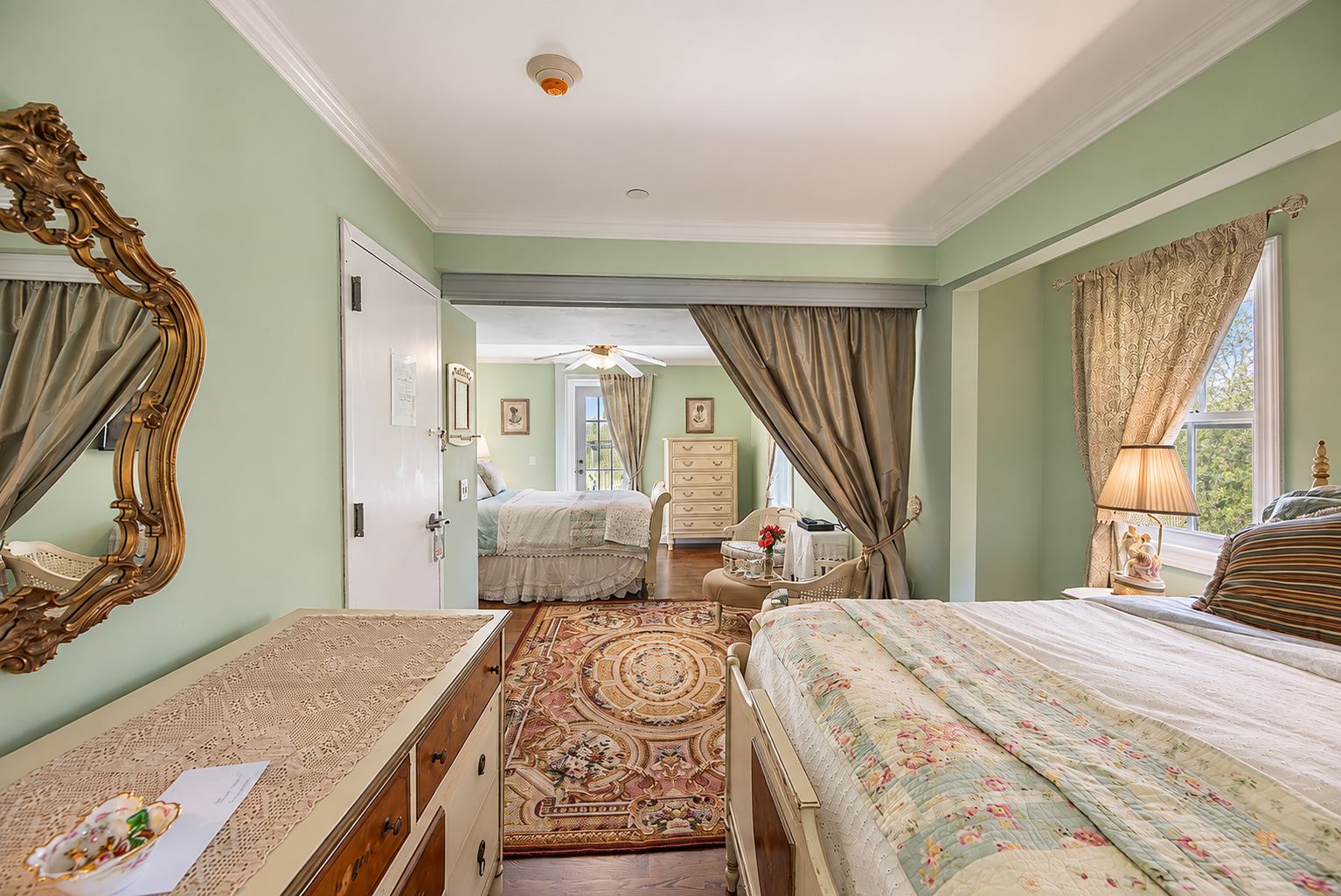 A bedroom with a large bed, a dresser, a mirror, and a view of another room.