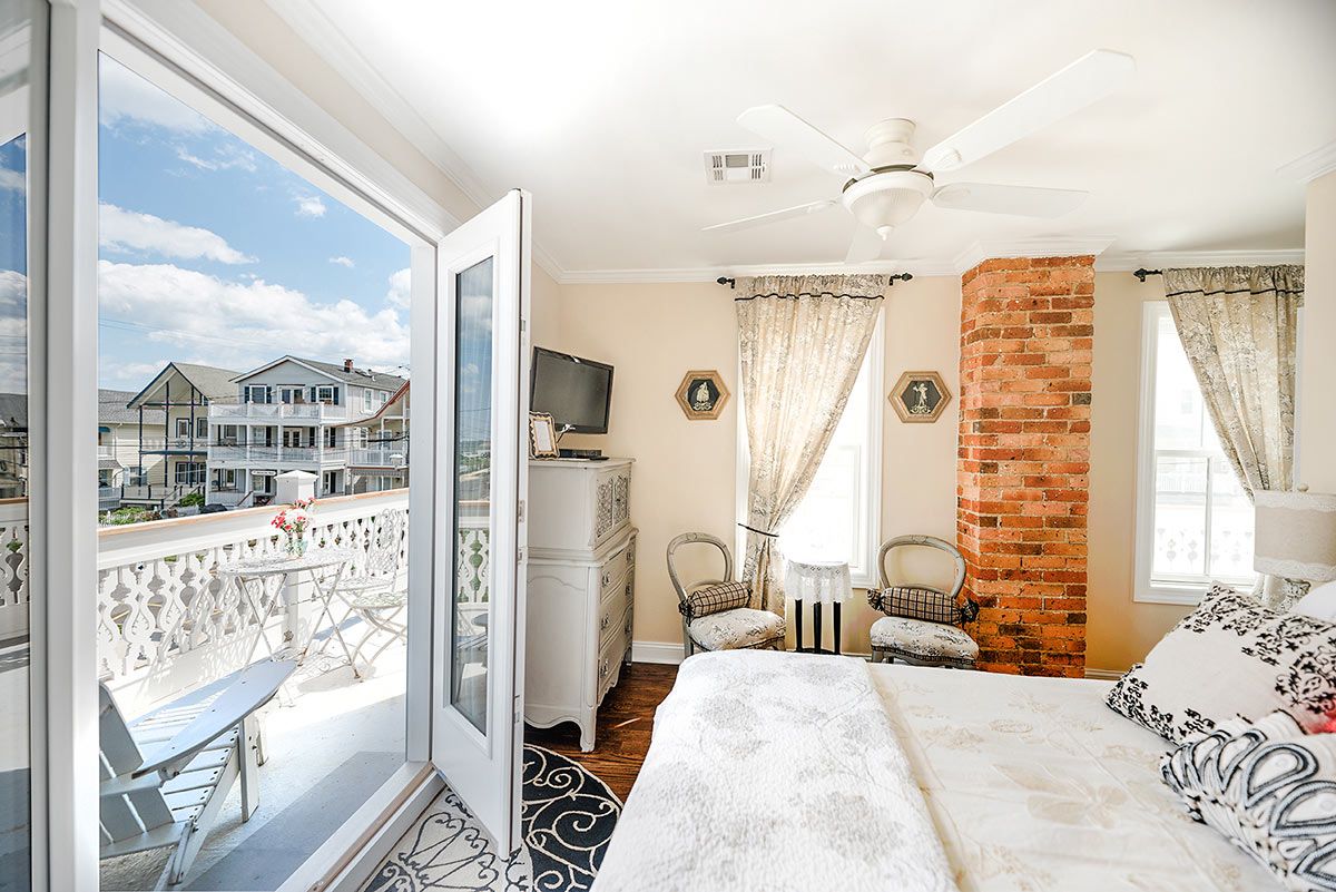 A bedroom with a balcony, a bed, a dresser, and a television.