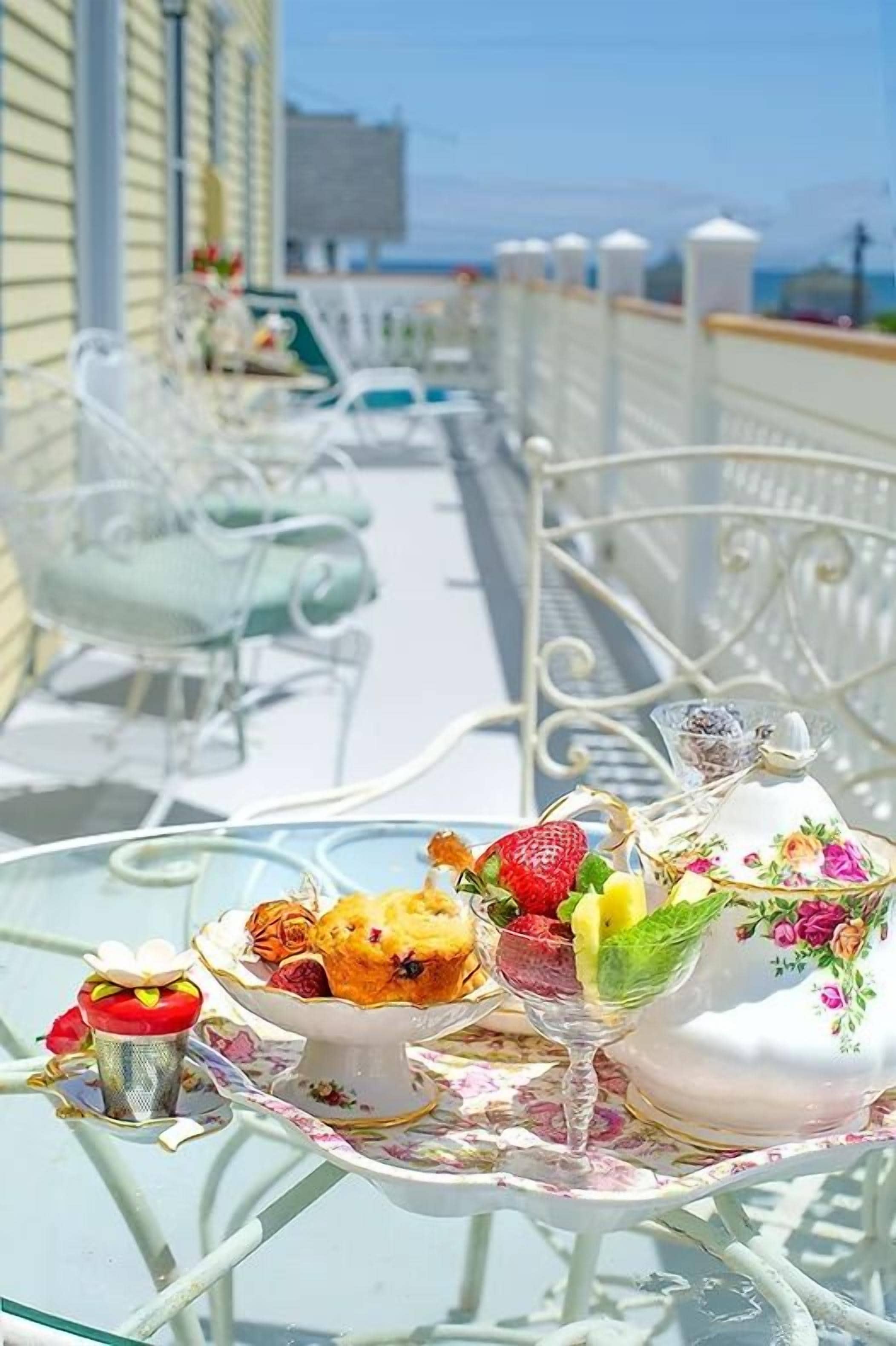 A sunlit outdoor dining area with tables and chairs, a railing, and a view of the sea.
