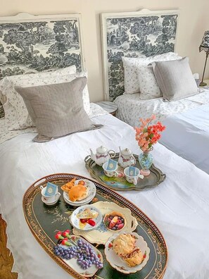 A hotel room with two beds, a tray with tea cups and pastries, and a vase with flowers. - The Carriage House B&B (Ocean Grove)