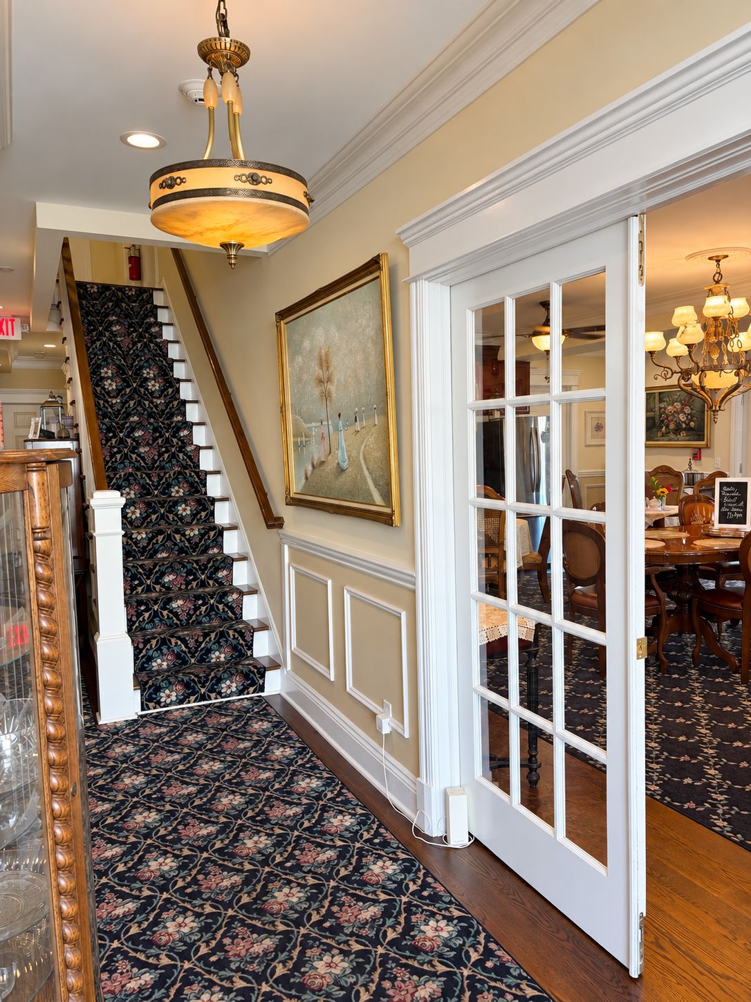 A staircase with a patterned carpet leading to a dining area with a chandelier.