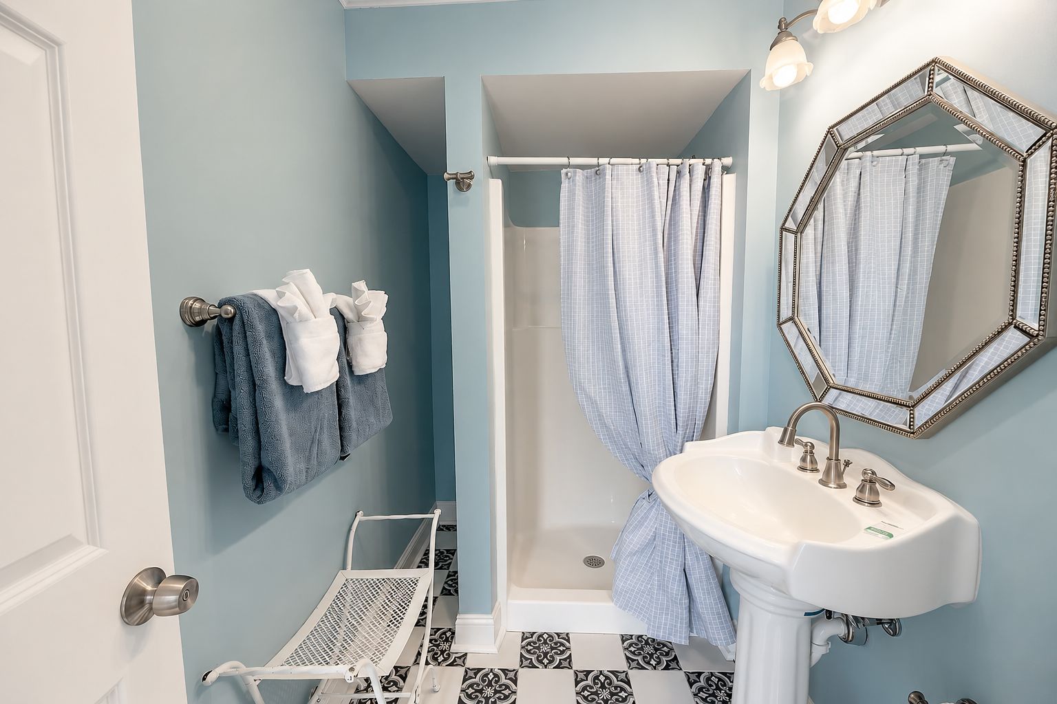 A bathroom with a white sink, a shower with a blue shower curtain, and a mirror with a decorative frame.