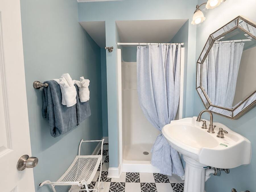 A bathroom with a white sink, a shower with a blue shower curtain, and a mirror with a decorative frame.