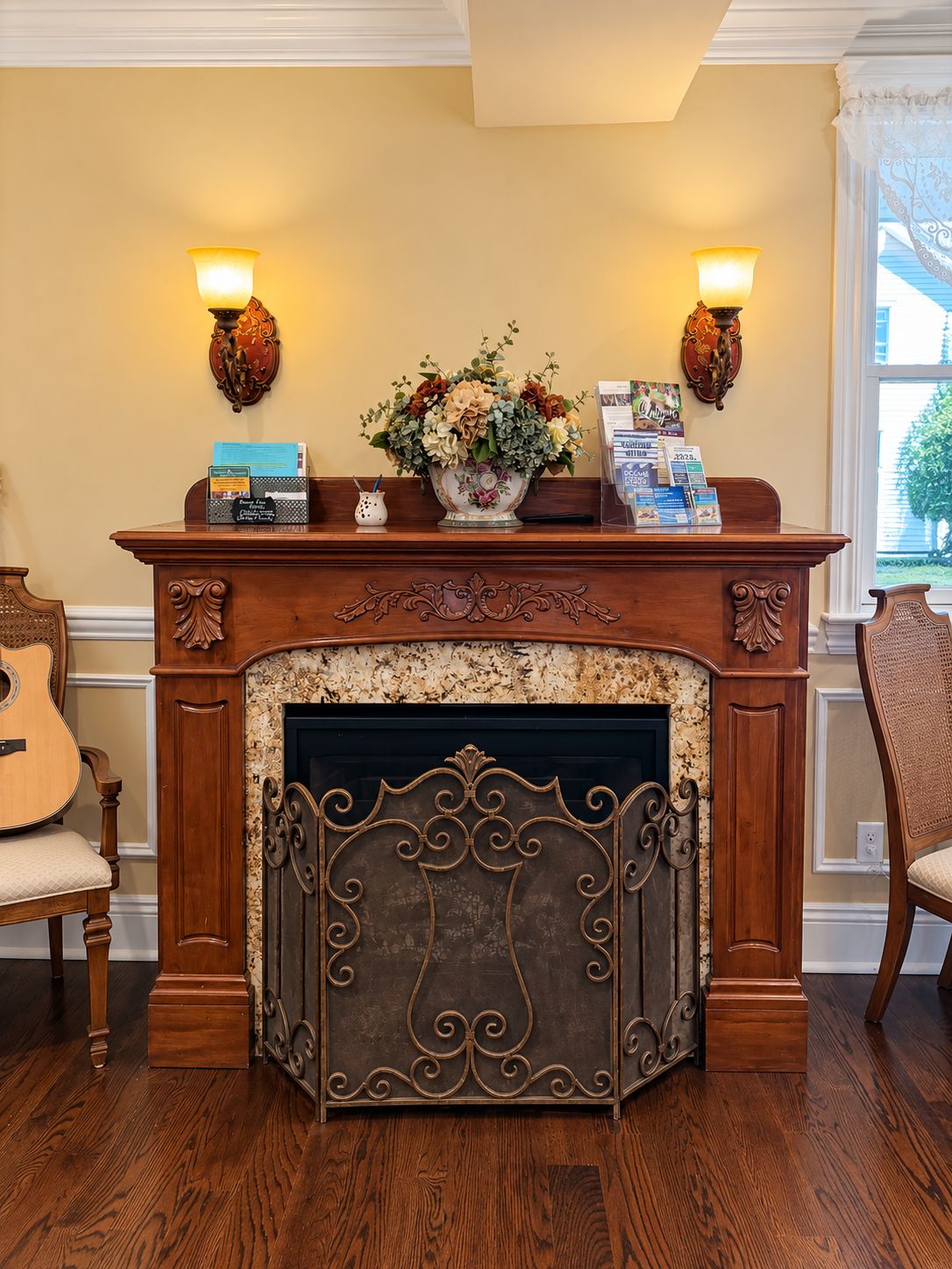 A fireplace with a decorative mantel, a vase of flowers, and two wall sconces.