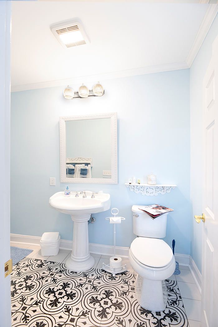 A bathroom with a pedestal sink, a toilet, a mirror, and patterned flooring.