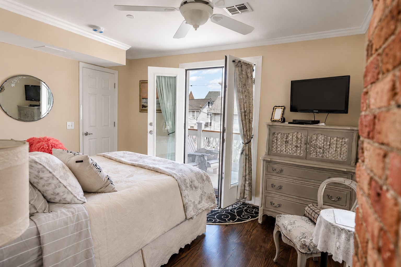 Une chambre à coucher avec un lit, une commode, un téléviseur et une vue sur l’extérieur, grâce à une porte ouverte.
