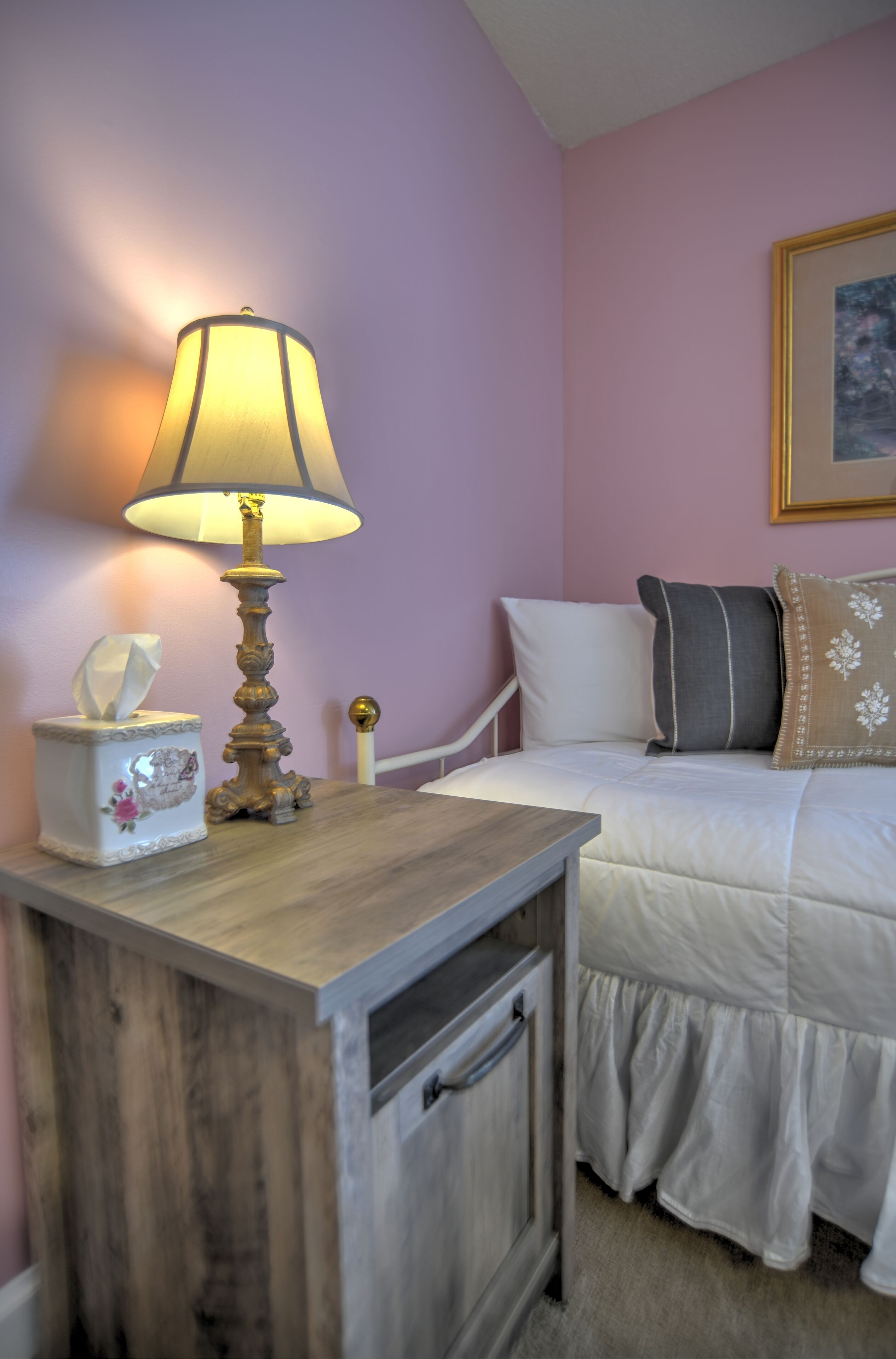 Une chambre à coucher avec une table de chevet en bois, une lampe, une boîte de mouchoirs et un lit avec une literie et des oreillers blancs.