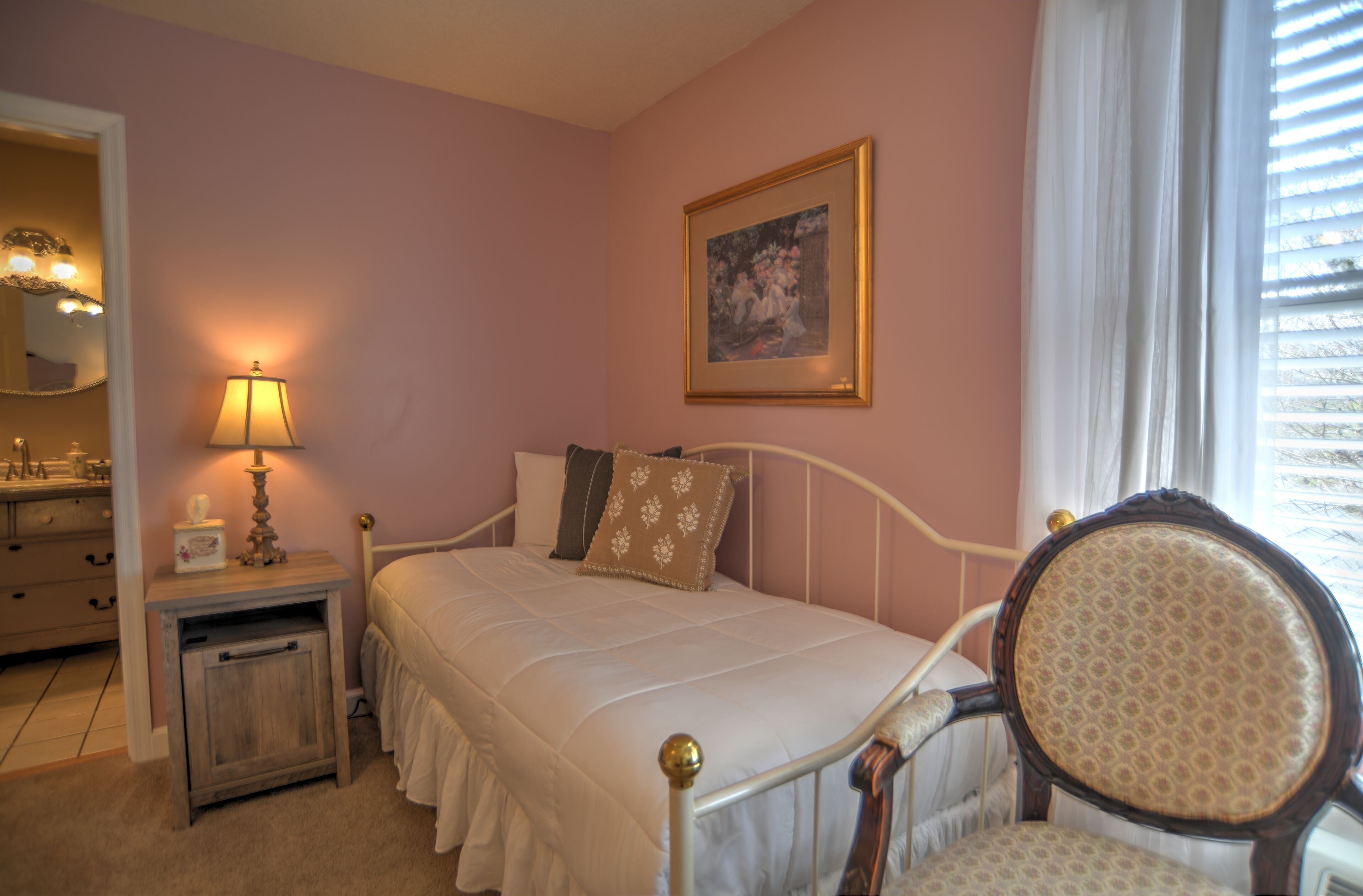 A bedroom with a bed, a chair, a bedside table with a lamp, a dresser, and a painting on the wall.