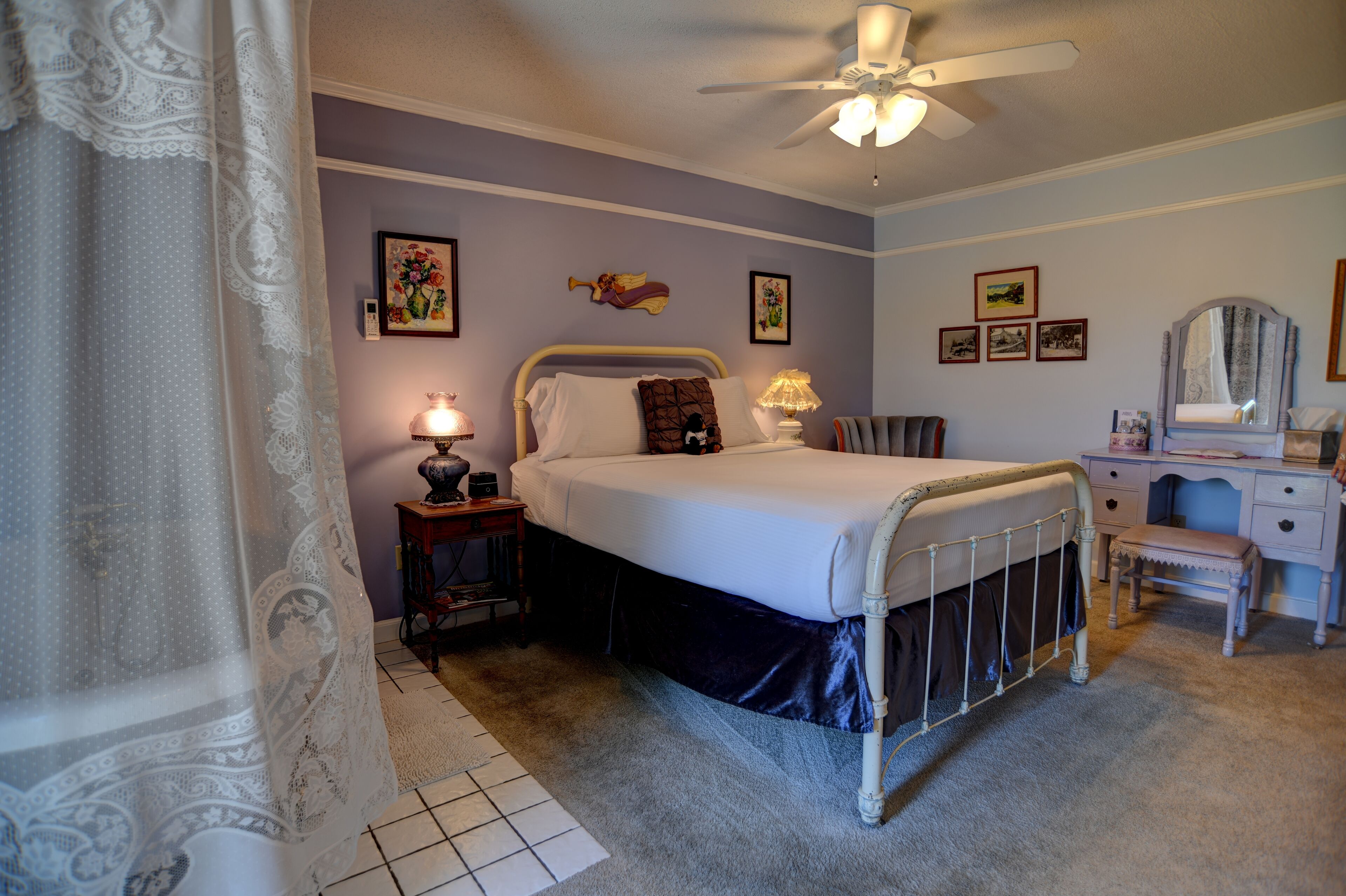 A bedroom with a bed, bedside tables, a desk, a chair, and a ceiling fan.