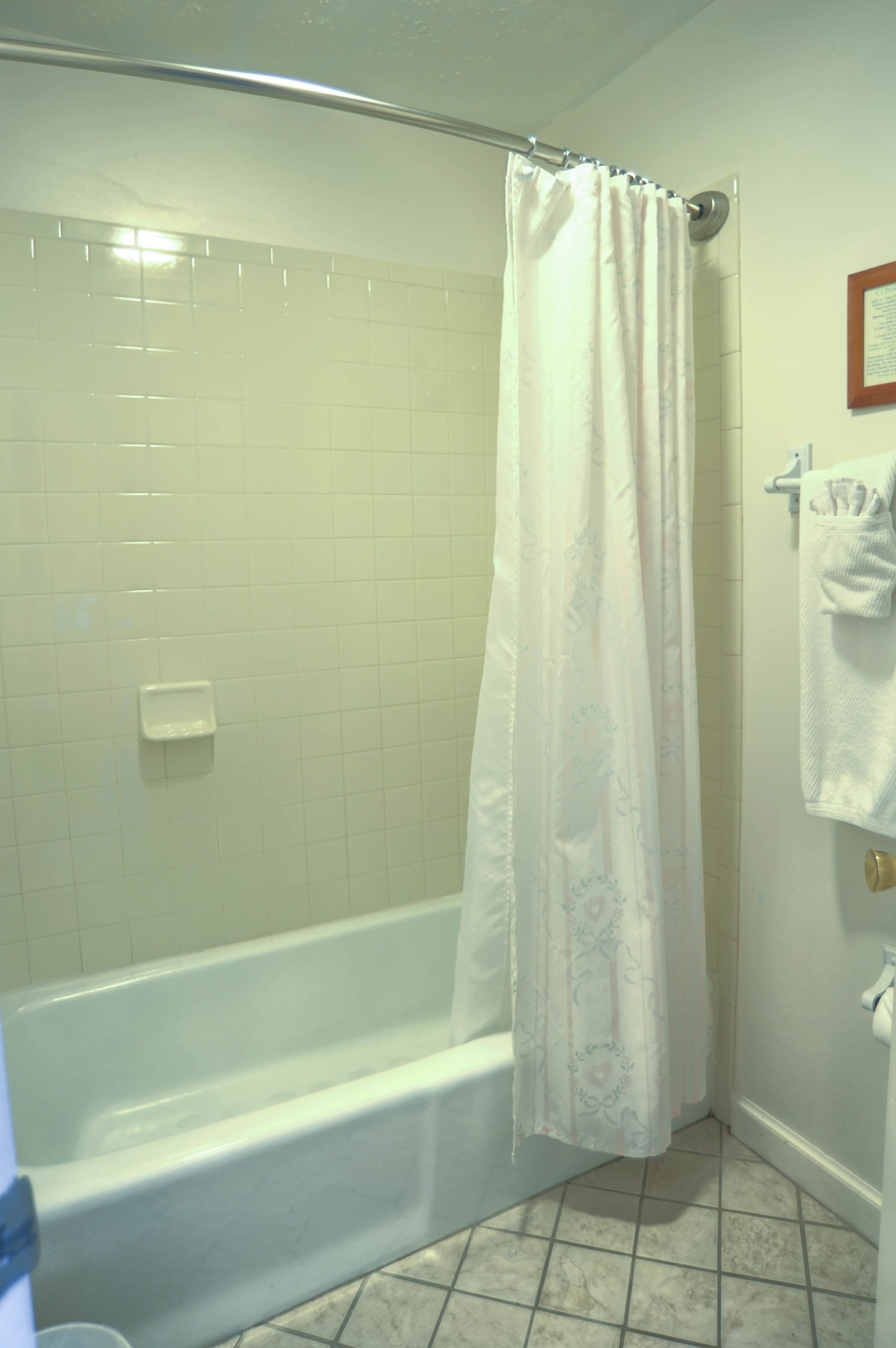 Un baño con una bañera blanca, una cortina de ducha y piso de baldosas.