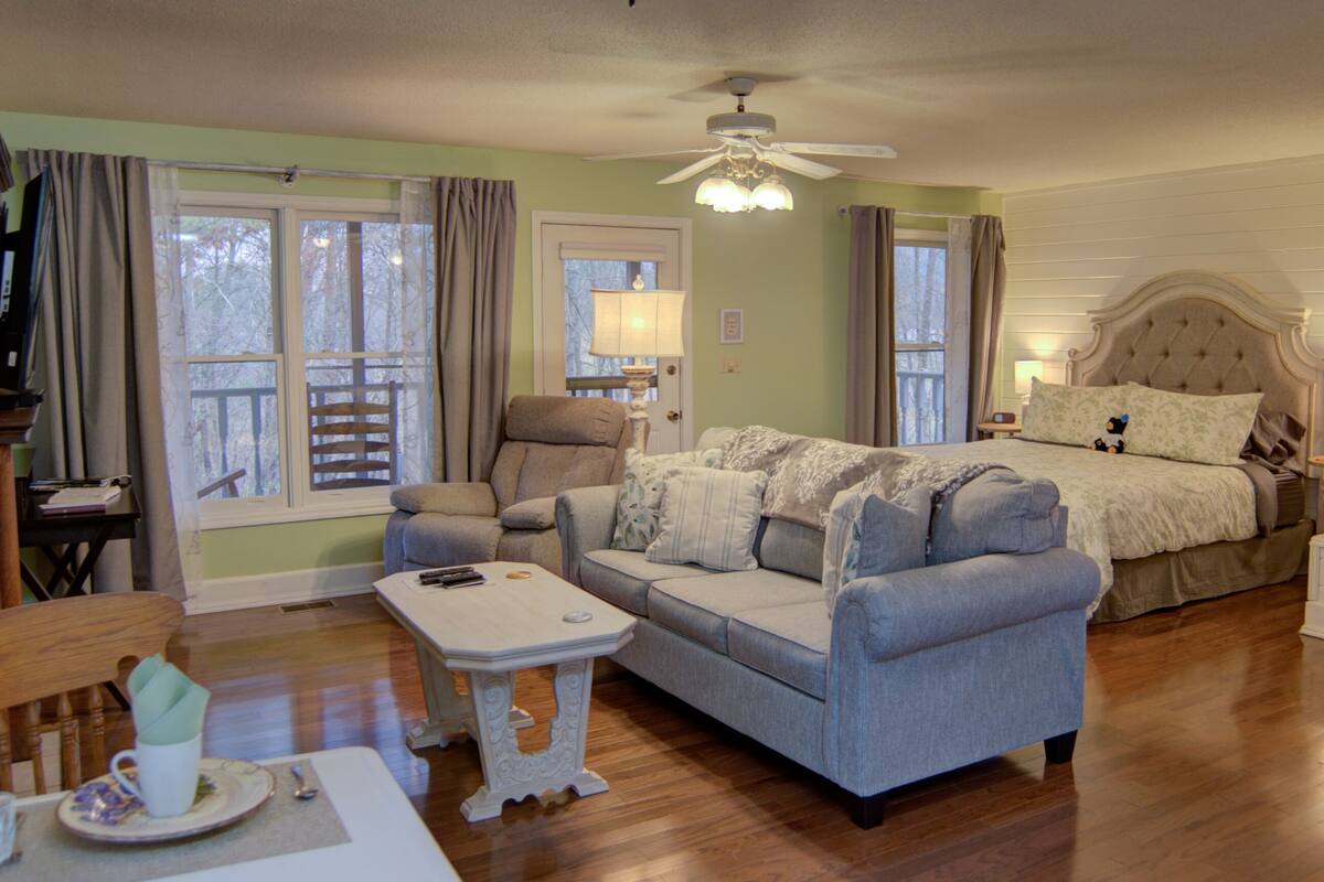 Une chambre à coucher comprenant un lit, un canapé, une chaise, une petite table et une fenêtre avec des rideaux.
