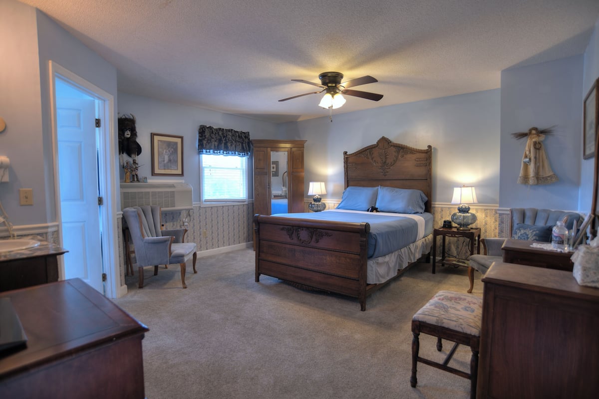 Une chambre à coucher avec un lit en bois, un ventilateur de plafond, une chaise, une table de chevet et une commode.