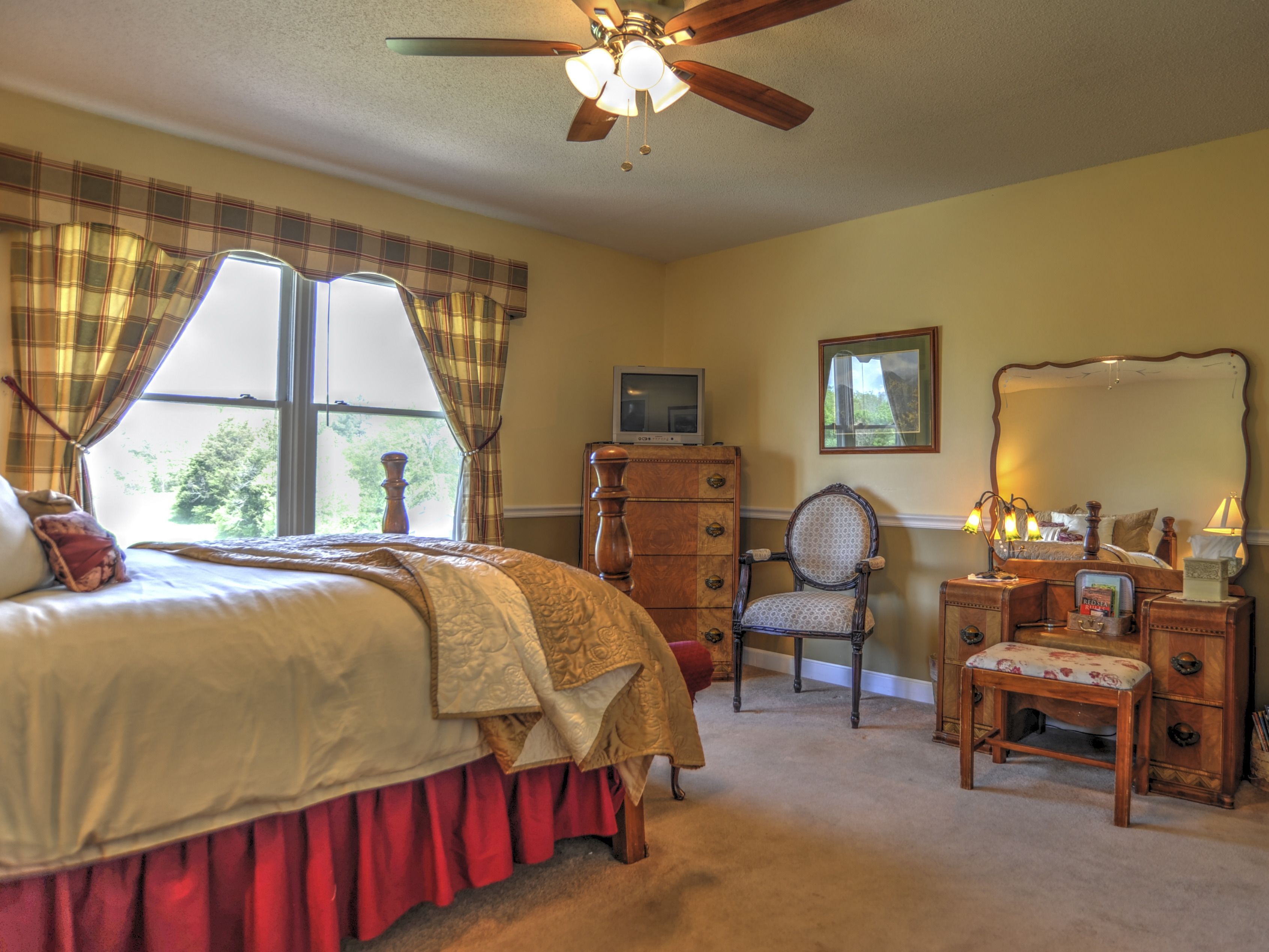 A bedroom with a bed, a dresser, a chair, a mirror, and a ceiling fan.