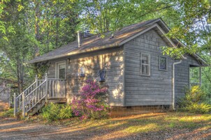 A wooden cabin with a covered porch, a staircase, and a small garden with pink flowers.