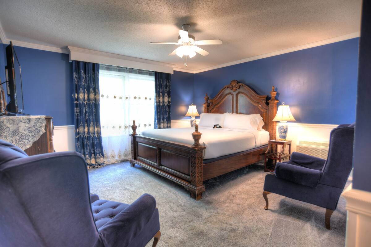 Une chambre à coucher avec un grand lit, deux fauteuils, un ventilateur de plafond et une table de chevet avec des lampes.