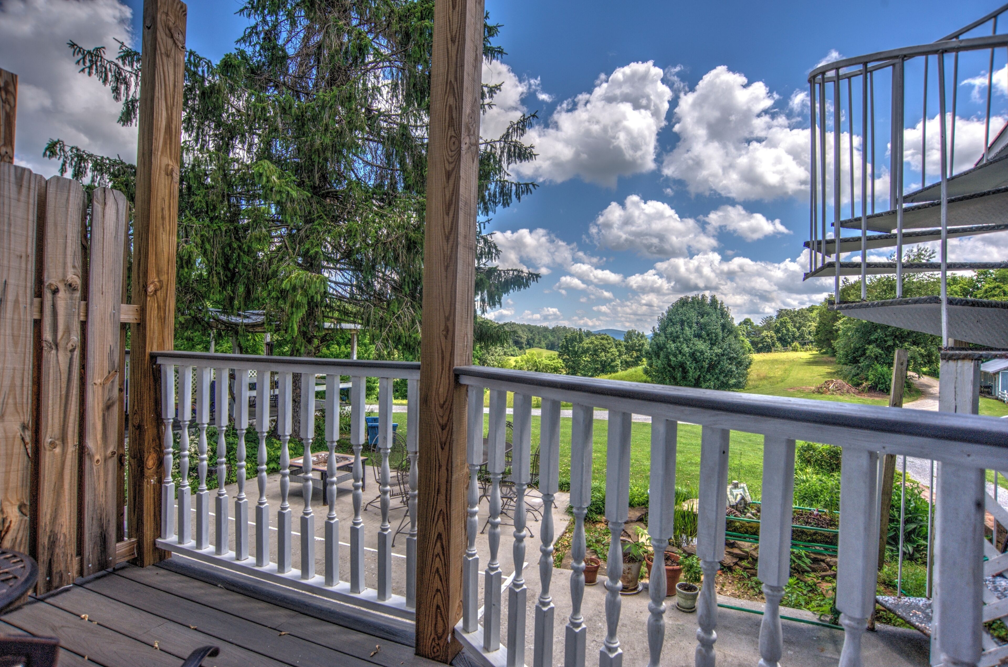 Eine Holzterrasse mit weißen Geländern, die auf einen gepflegten Garten und einen strahlend blauen Himmel blickt.