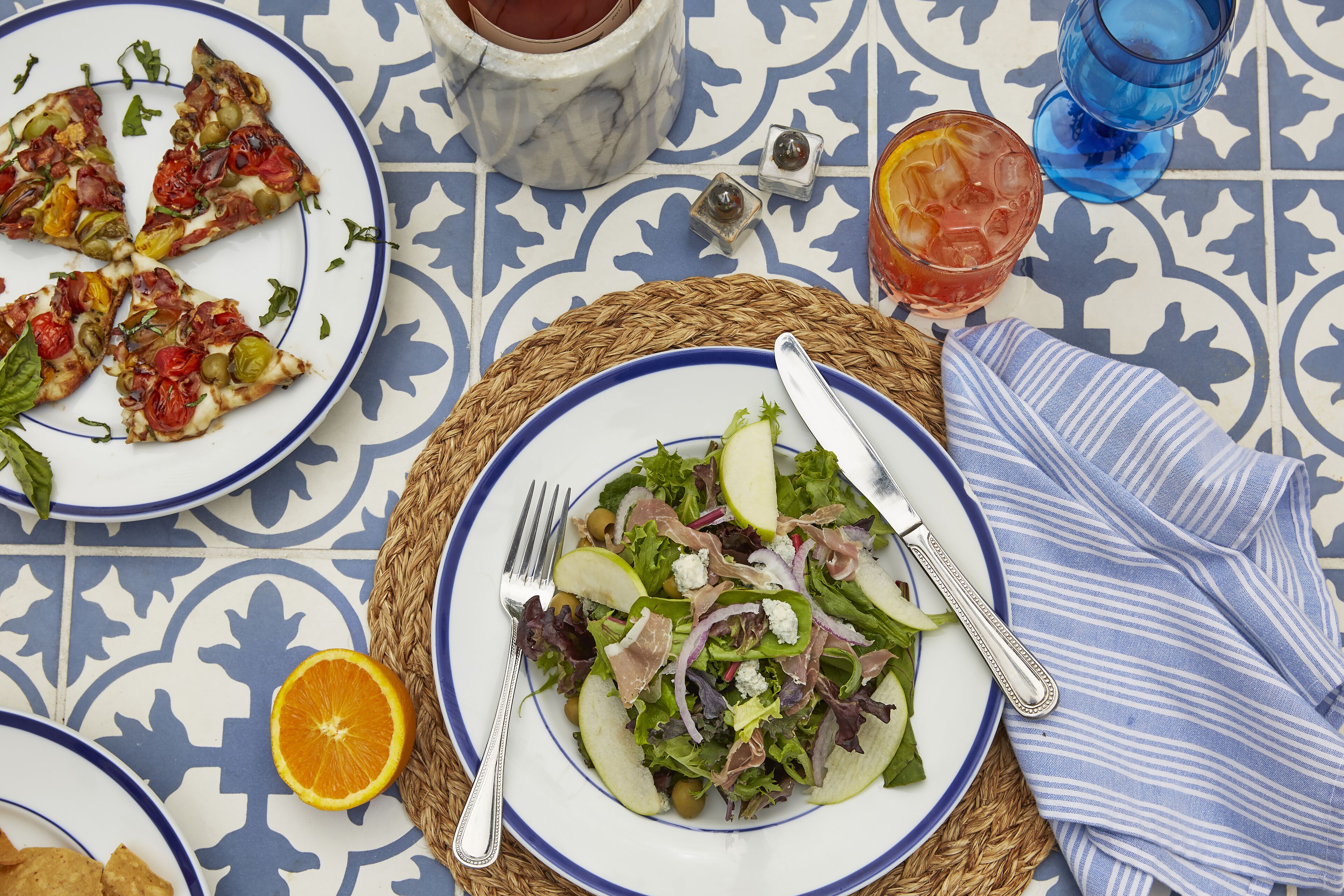 Una mesa con una ensalada, una porción de pizza, un vaso de bebida helada y una taza de té.