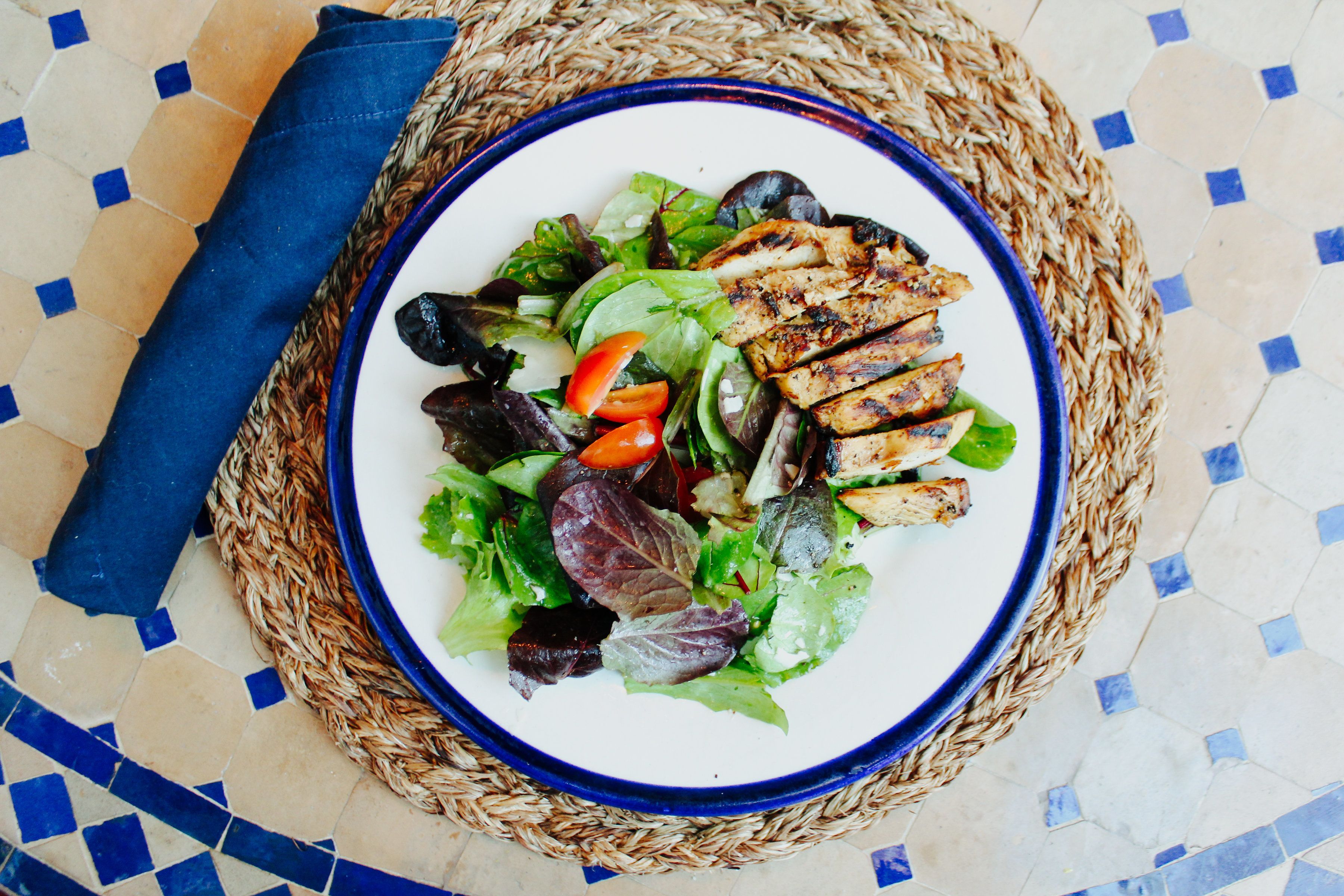 A plate of grilled chicken and salad on a woven mat.